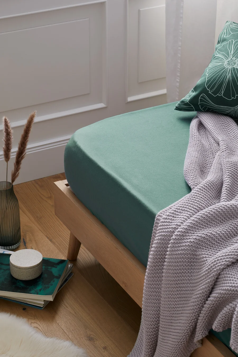 Grünes Biber-Spannbettlaken auf einem Bett mit einer Strickdecke darüber.