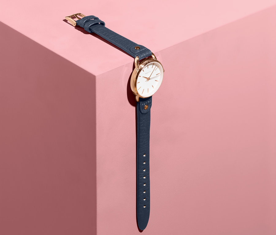 Damenuhr mit Lederarmband liegt auf einem rosa Sockel.