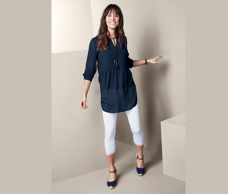 Frau posiert in Longbluse und weißen Leggings.