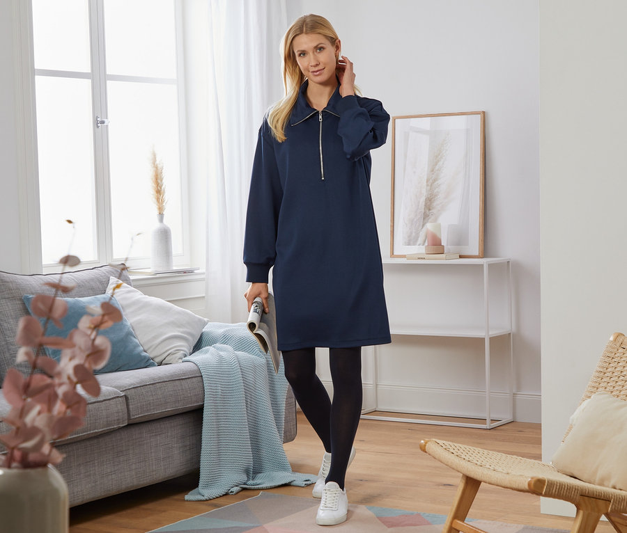 Frau posiert im Wohnzimmer und trägt ein Sweatkleid.