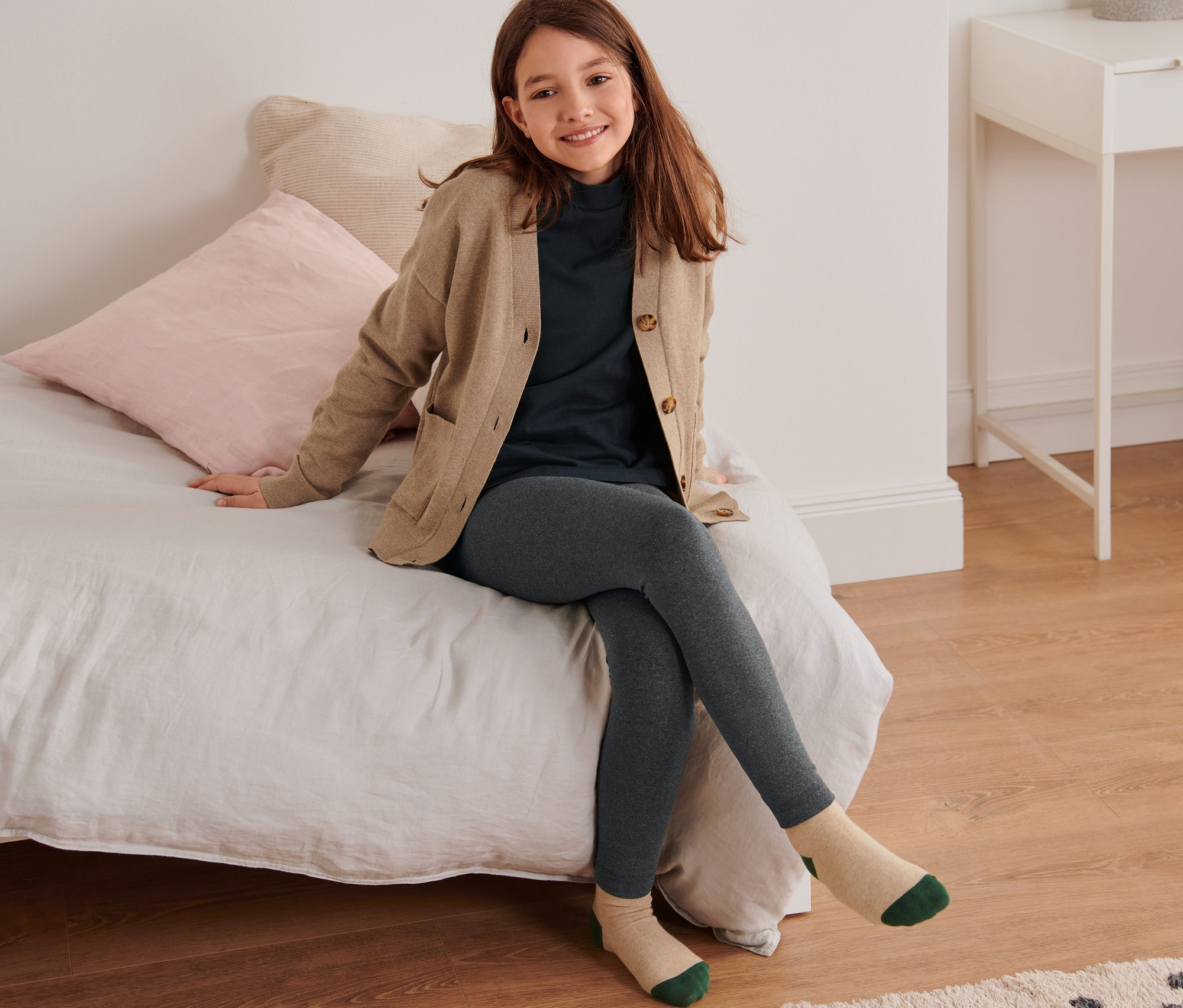 Ein Mädchen sitzt auf einem Bett und trägt eine Kinder-Thermoleggings.