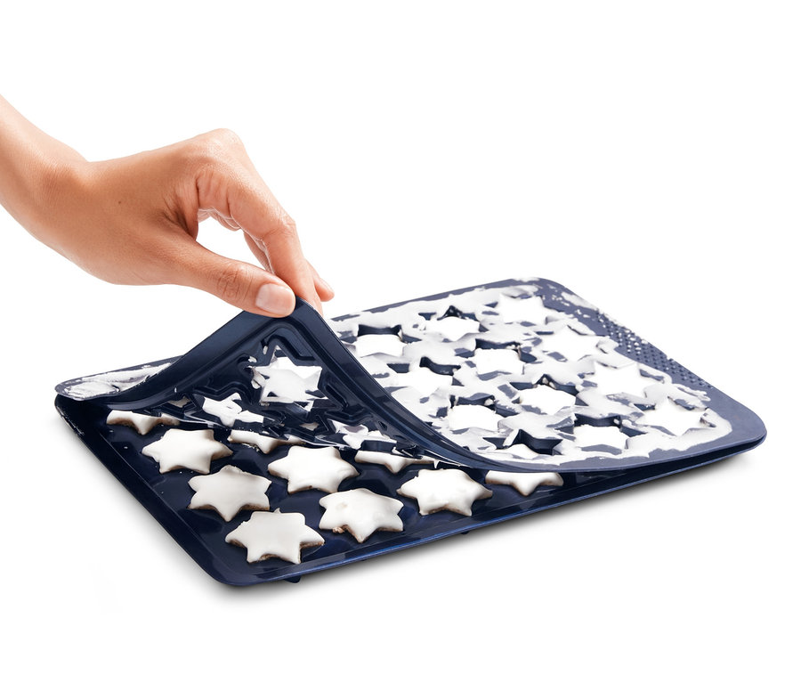 Eine Hand entfernt die Zimtstern-Backmatte mit weißen Sternen.