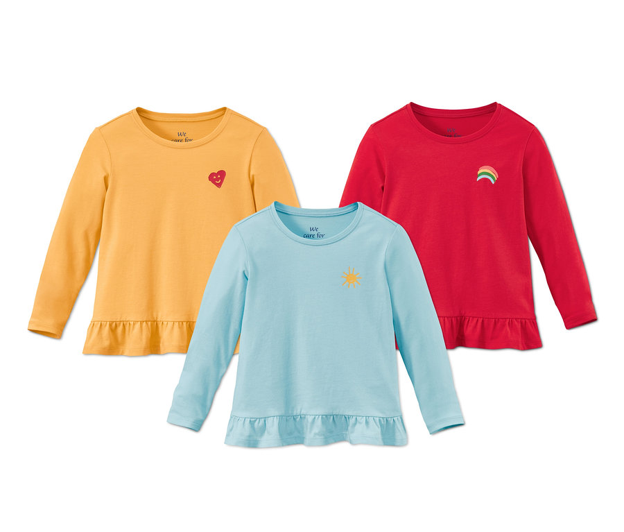Drei Shirts aus Bio-Baumwolle: ein gelbes mit Herzmotiv, ein blaues mit Sonnenmotiv und ein rotes mit Regenbogenmotiv.