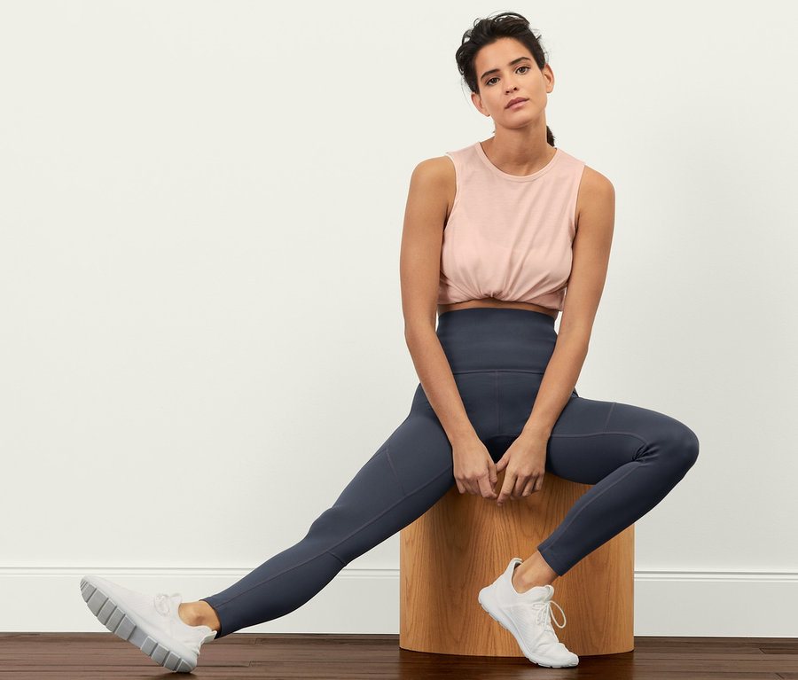 Frau sitzt auf einem Holzhocker und trägt eine Sporttight »Sculpture«, ein Top und Turnschuhe.