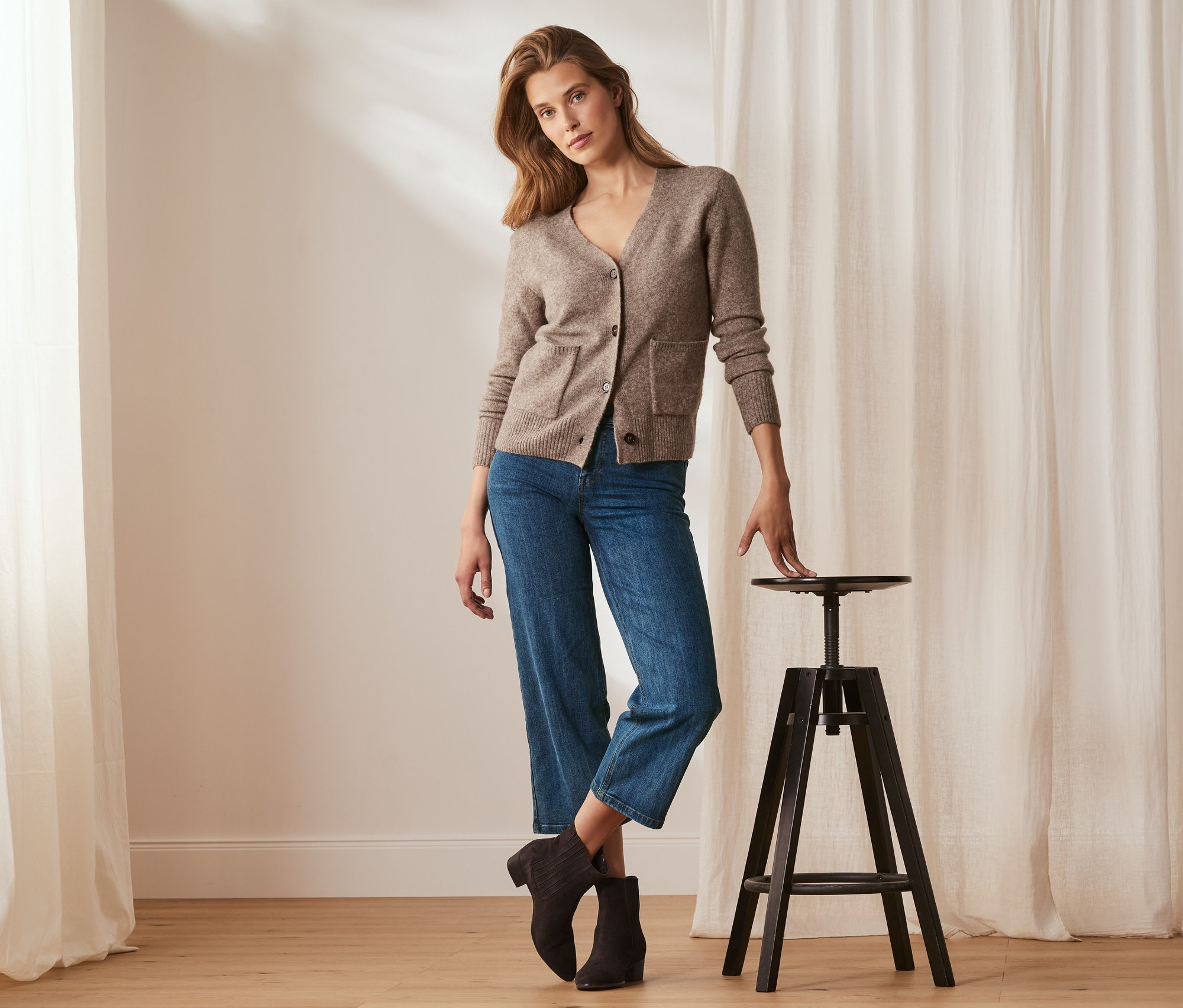 Frau posiert in braunem Cardigan und Jeans in verkürzter Länge.