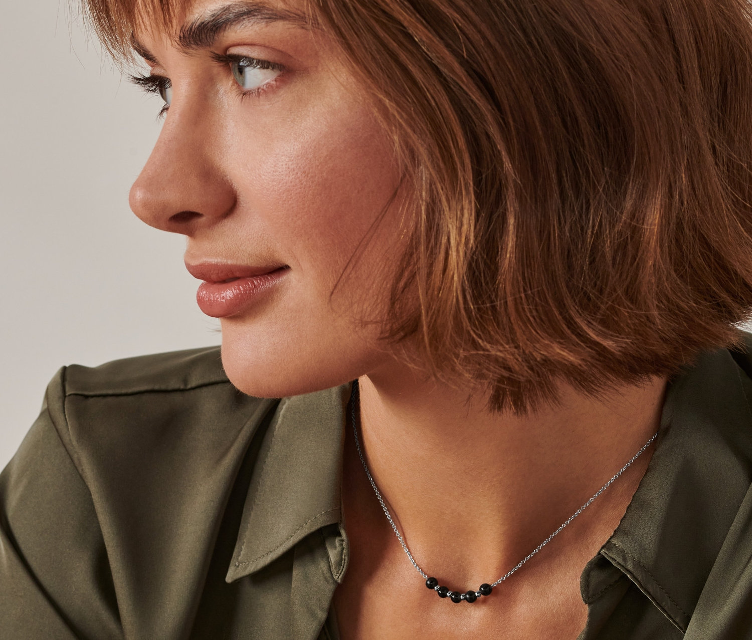 Profil einer Frau mit braunen Haaren und einem grünen Hemd, die eine Energie-Obsidian-Kette trägt.