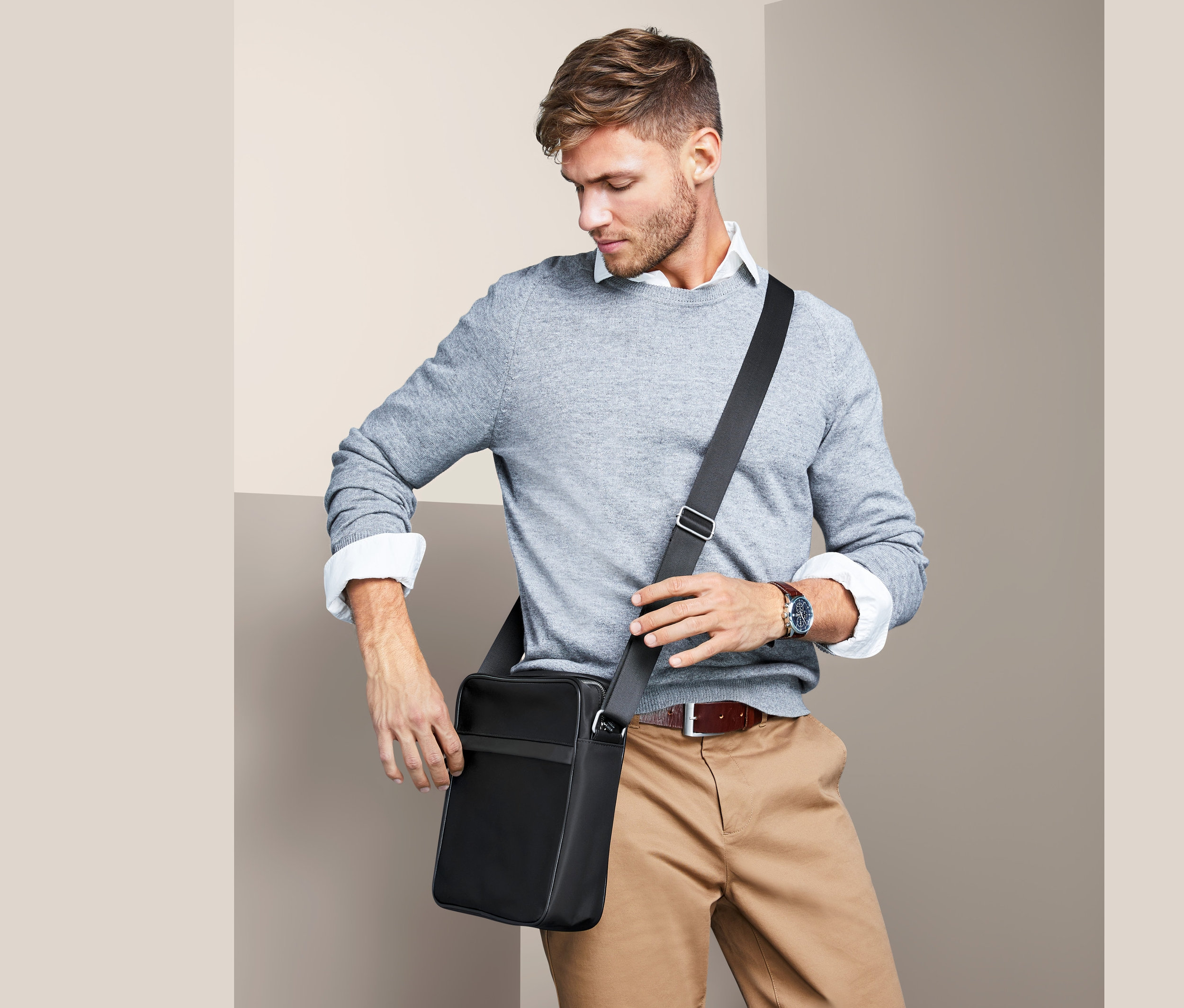 Mann mit grauem Pullover und beigen Hosen schaut auf eine schwarze Crossbag.