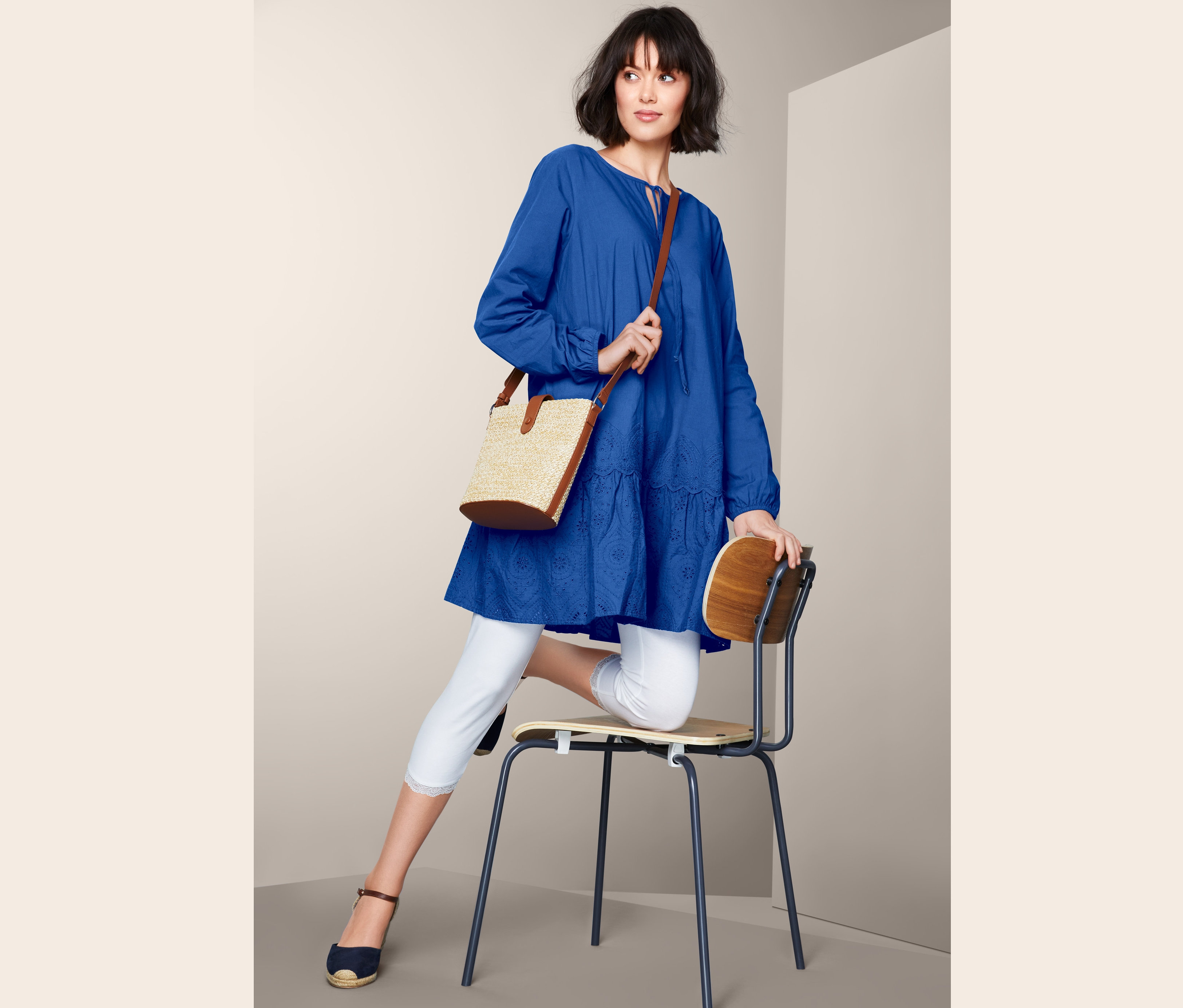 Frau posiert auf einem Stuhl in blauer Longbluse mit Stickerei.