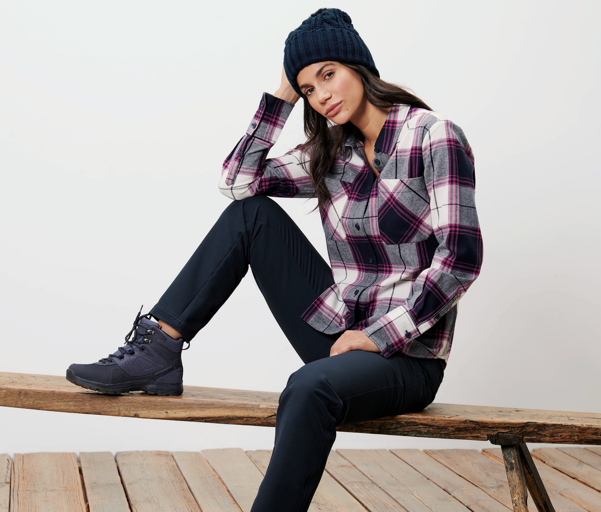Frau sitzt auf Bank, trägt Karo-Bluse und Strickmütze.