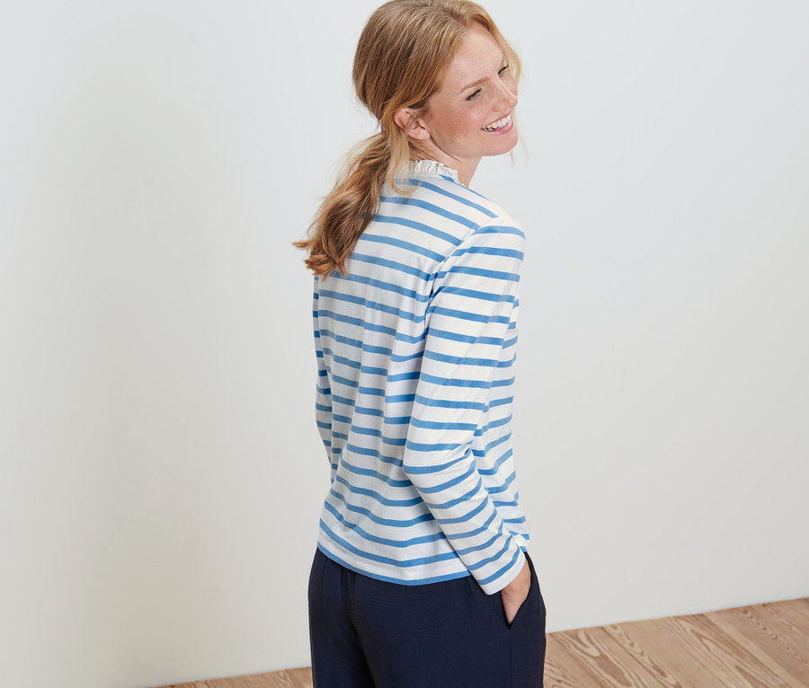 Frau posiert in einem Langarmshirt mit Rüschen.