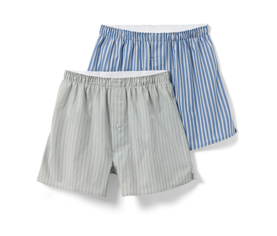 Zwei Web-Boxershorts, eine hellgrau mit weißen Streifen und Knopf, die andere blau mit weißen Streifen.