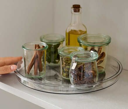 Hand greift nach Drehplatte mit Gewürzen im Regal.