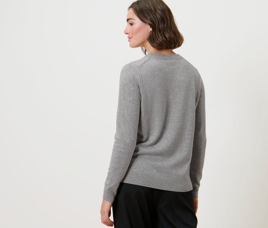 Frau schaut über die Schulter und trägt einen grau melierten Feinstrickpullover mit Cashmere.
