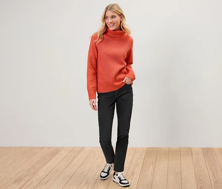 Eine Frau posiert in einem orangefarbenen Pullover und einer schwarzen Slim Jeans – Fit »Emma«.