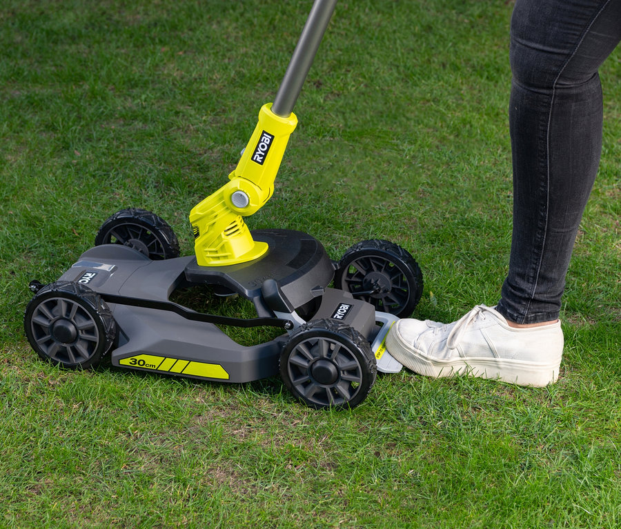 Eine Frau schiebt mit dem Fuß einen RYOBI 18 V One+ Akku-City-Rasenmäher auf dem Rasen.