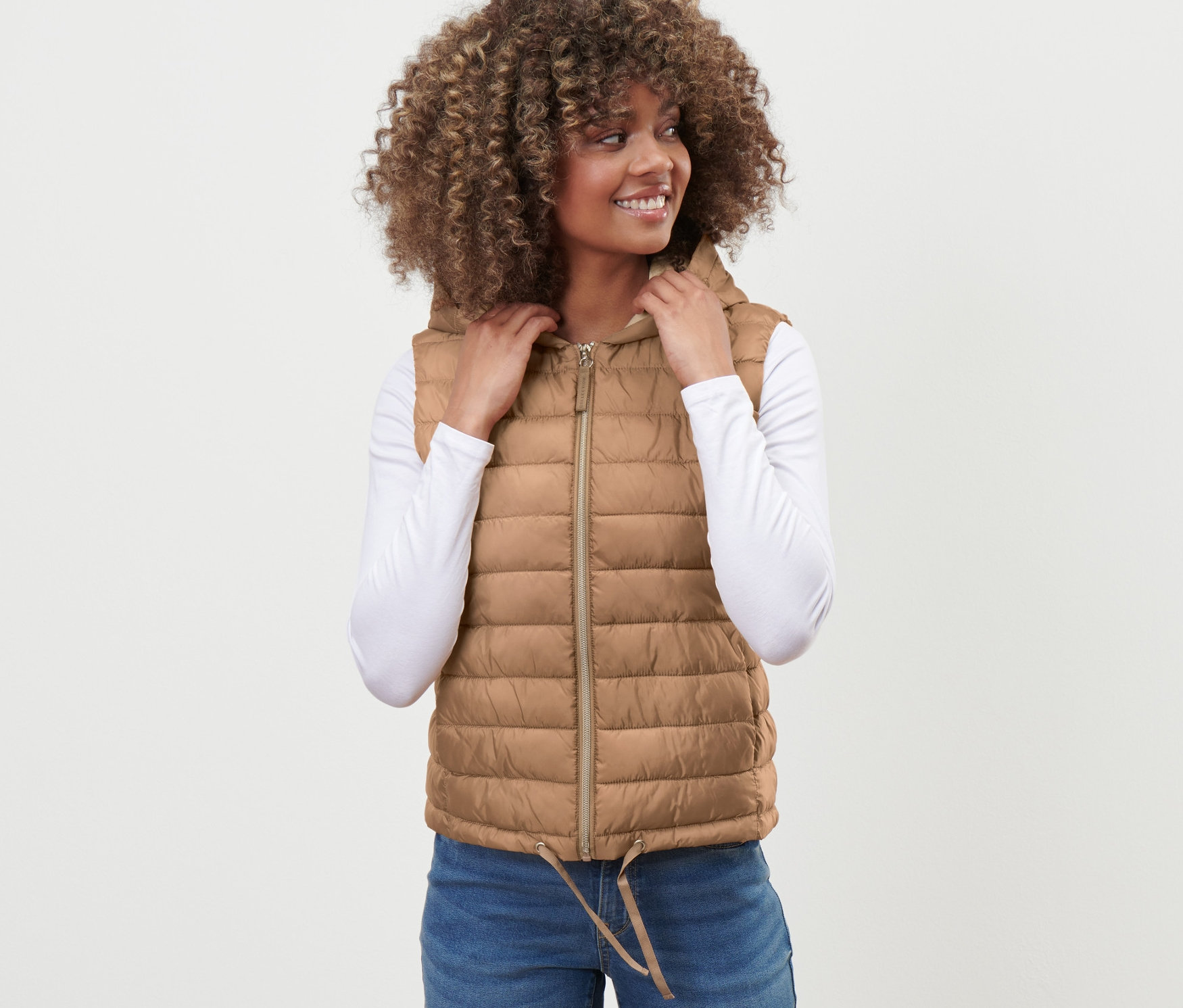 Frau trägt eine Steppweste mit Kapuze, Jeans und ein weißes Shirt.