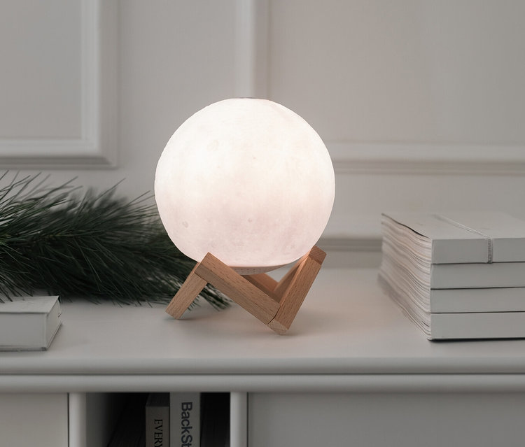 Leuchtender LED-Bluetooth®-Lautsprecher »Mond« steht auf einem Tisch neben Büchern und Tannenzweigen.