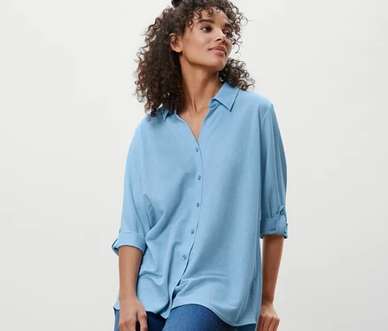 Eine Frau sitzt auf einem Hocker und trägt eine hellblaue Piqué-Jerseybluse und Jeans.