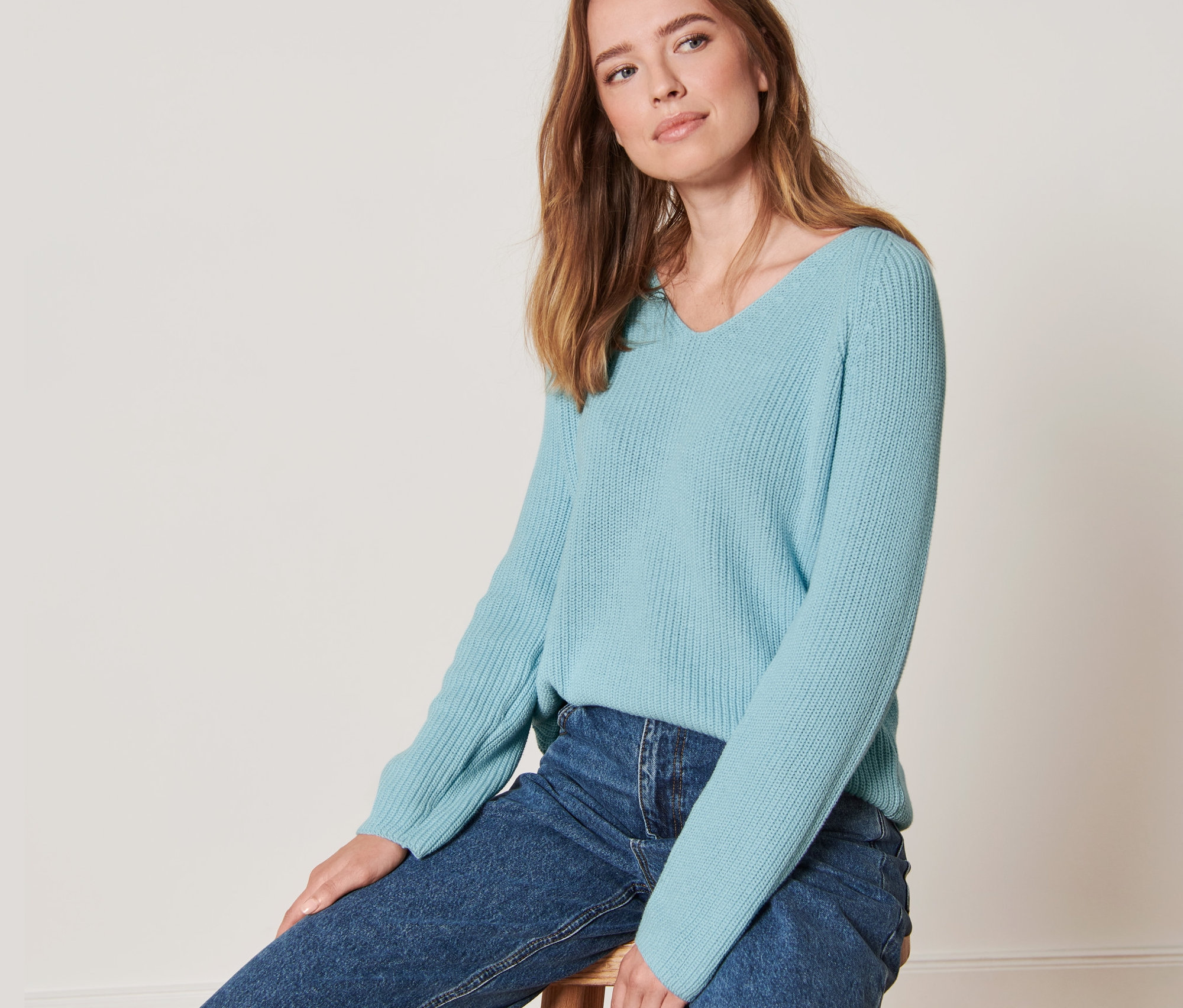 Frau sitzt auf einem Hocker und trägt einen hellblauen Strickpullover.