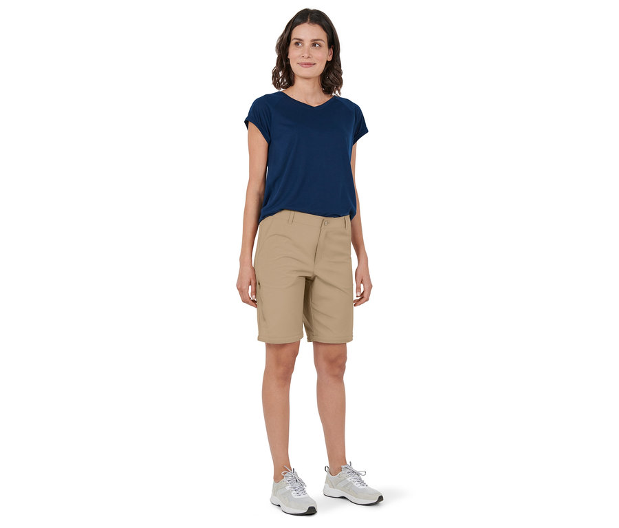 Eine Frau steht und trägt eine creme 2-in-1-Funktionshose, ein marineblaues T-Shirt und Turnschuhe.