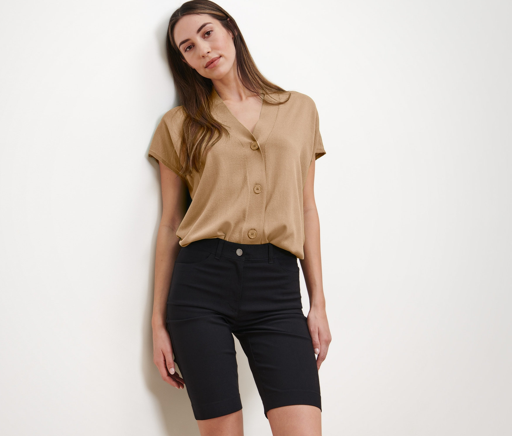Frau posiert in beiger Bluse und schwarzen Bengalin-Bermudashorts.