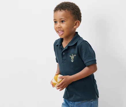 Junge trägt eines von 2 Kinder-Poloshirts aus Baumwoll-Piqué und hält einen Ball.
