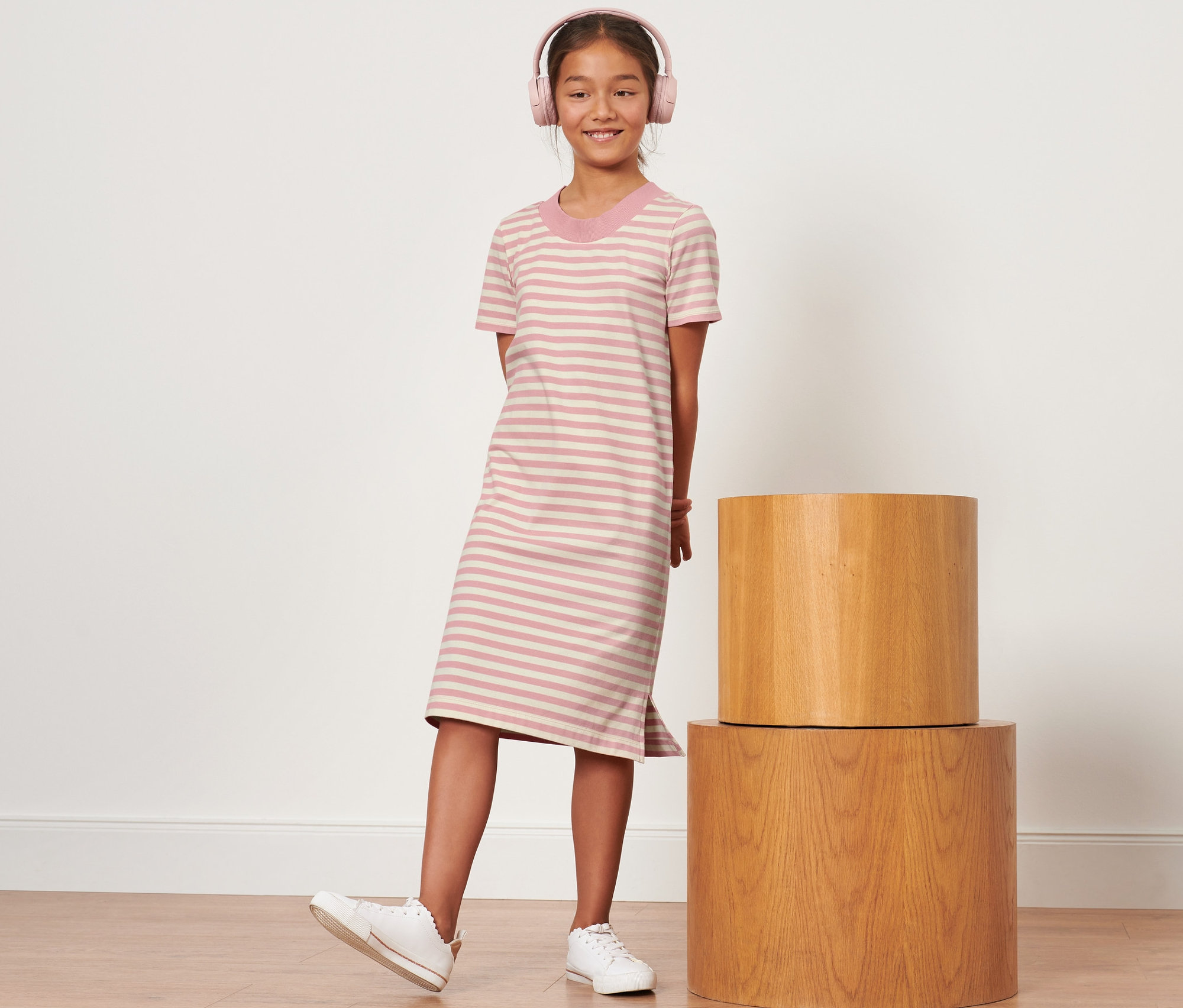 Mädchen mit rosa Kopfhörern steht in einem gestreiften Kinder-Jerseykleid.