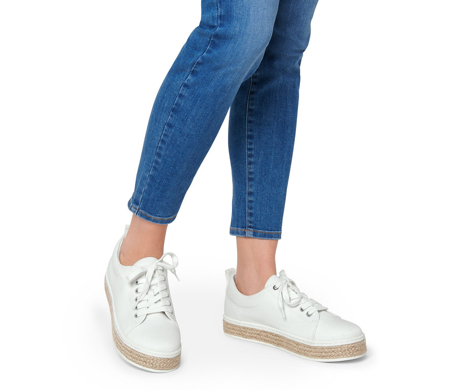 Beine einer Frau in Jeans und weißen Canvas-Sneakern.