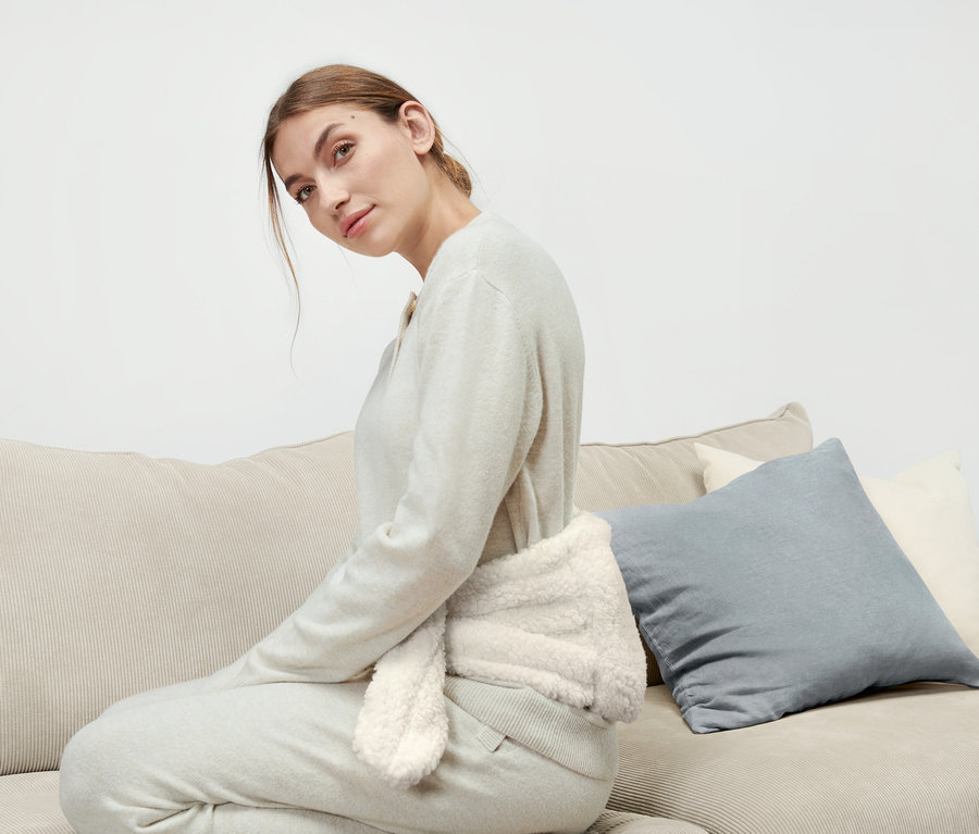 Eine Frau sitzt auf einem Sofa und trägt eine Wärmflasche mit Band um ihre Taille.