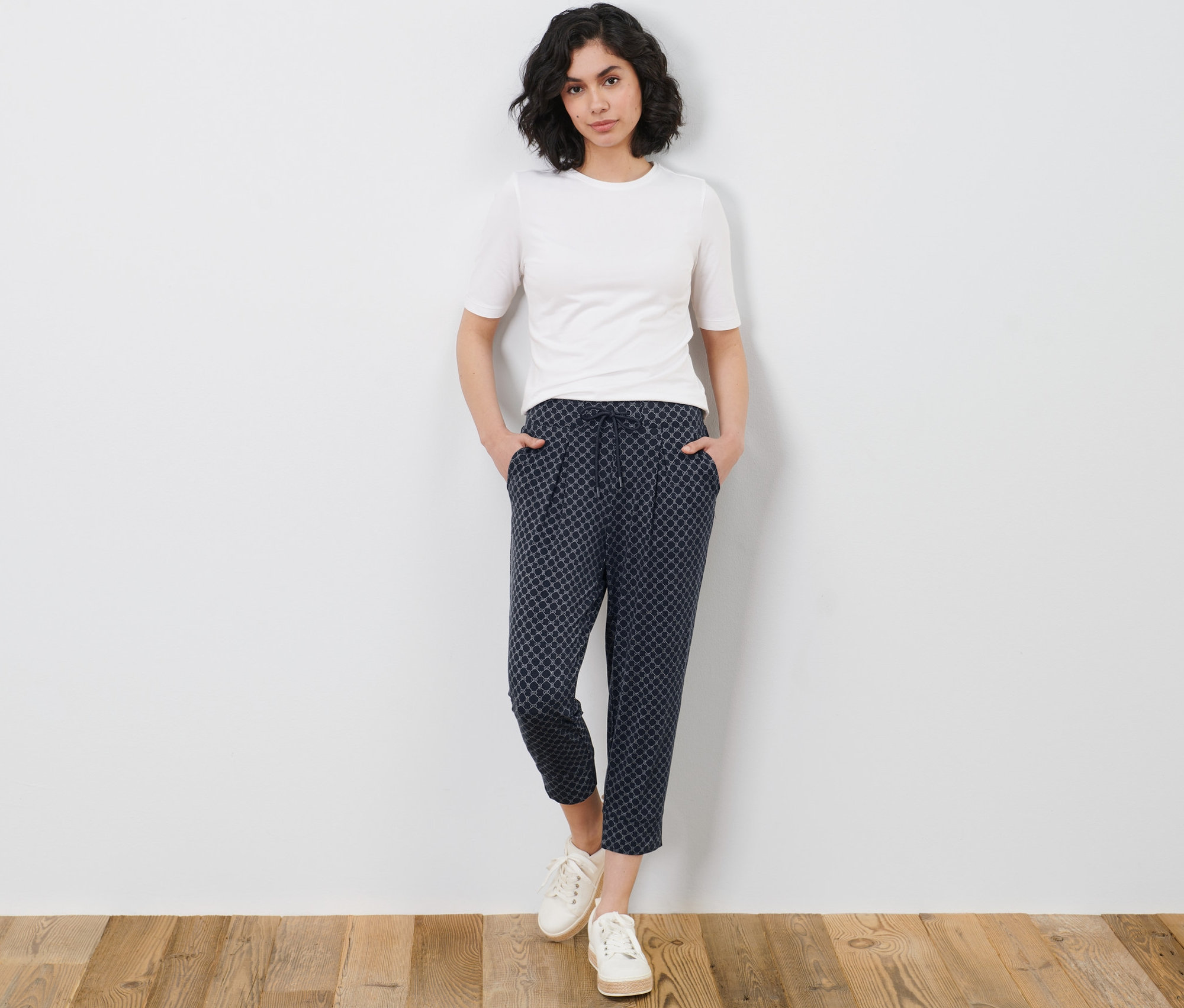 Frau posiert in einem weißen T-Shirt und einer bedruckten 3/4-Jerseyhose.