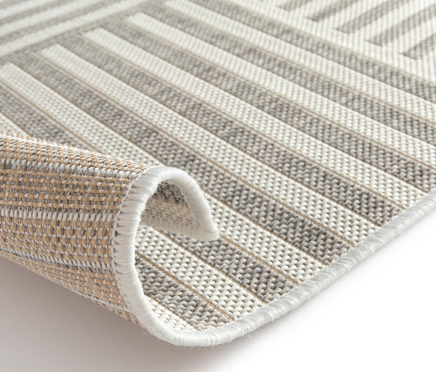 Detailansicht eines beigen Outdoor-Teppichs »Lines« mit geometrischem Muster und aufgerollter Ecke.