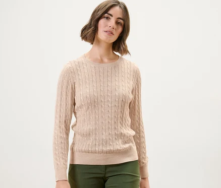 Frau trägt einen cremefarbenen Zopfstrickpullover.