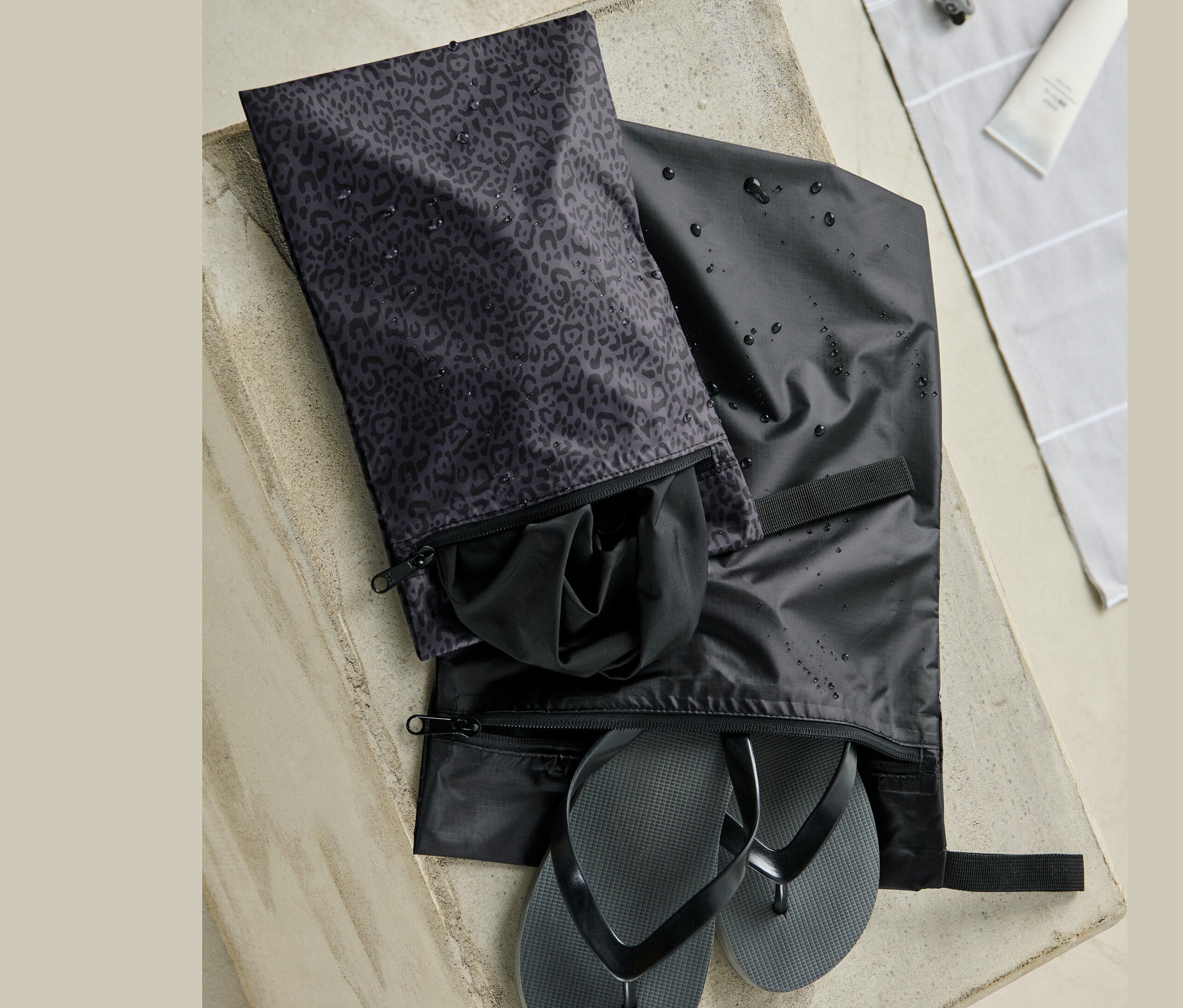 Zwei wasserfeste Packsäcke auf Betonoberfläche. In einem sind schwarze Zehentrenner, im anderen schwarze Kleidung.