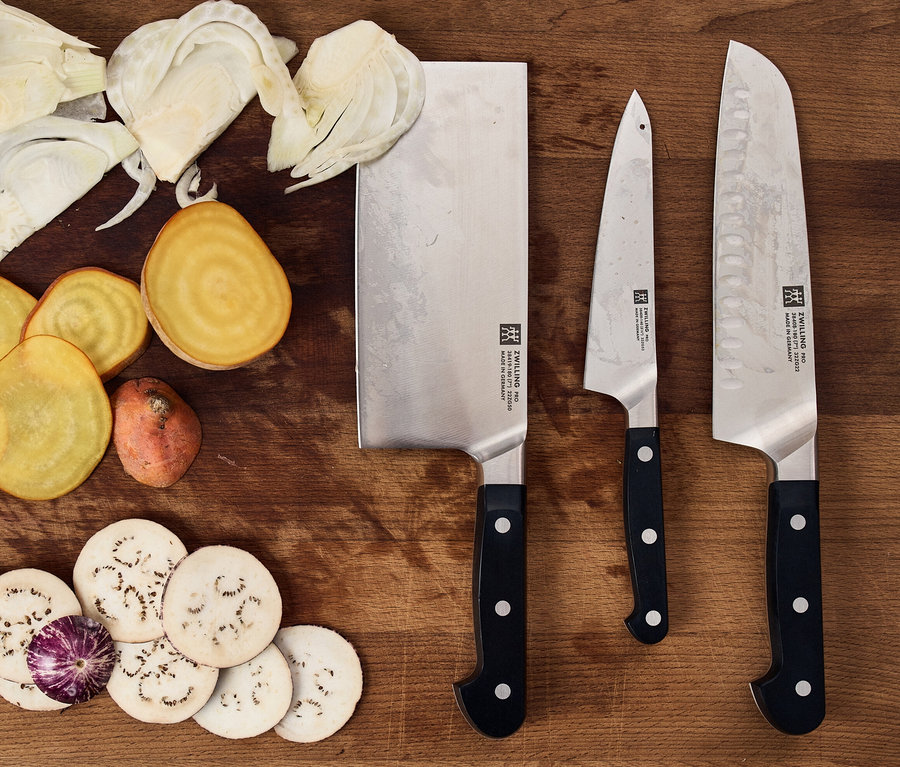 Auf einem Holzbrett liegen geschnittenes Gemüse und ein ZWILLING PRO Messerblock, selbstschärfend, 7-teilig.