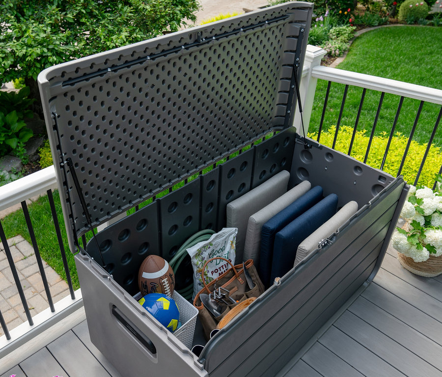Geöffnete Aufbewahrungsbox, 625 l, graubraun auf einer Terrasse, gefüllt mit Kissen, Bällen und Gartenzubehör.