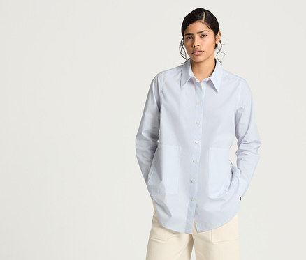 Frau trägt eine blaue NAH/STUDIO Longbluse aus Bio-Baumwolle, eine NAH/STUDIO Culotte aus ungefaerbter Baumwolle und eine NAH/STUDIO Mantelweste aus recycelter Wolle.