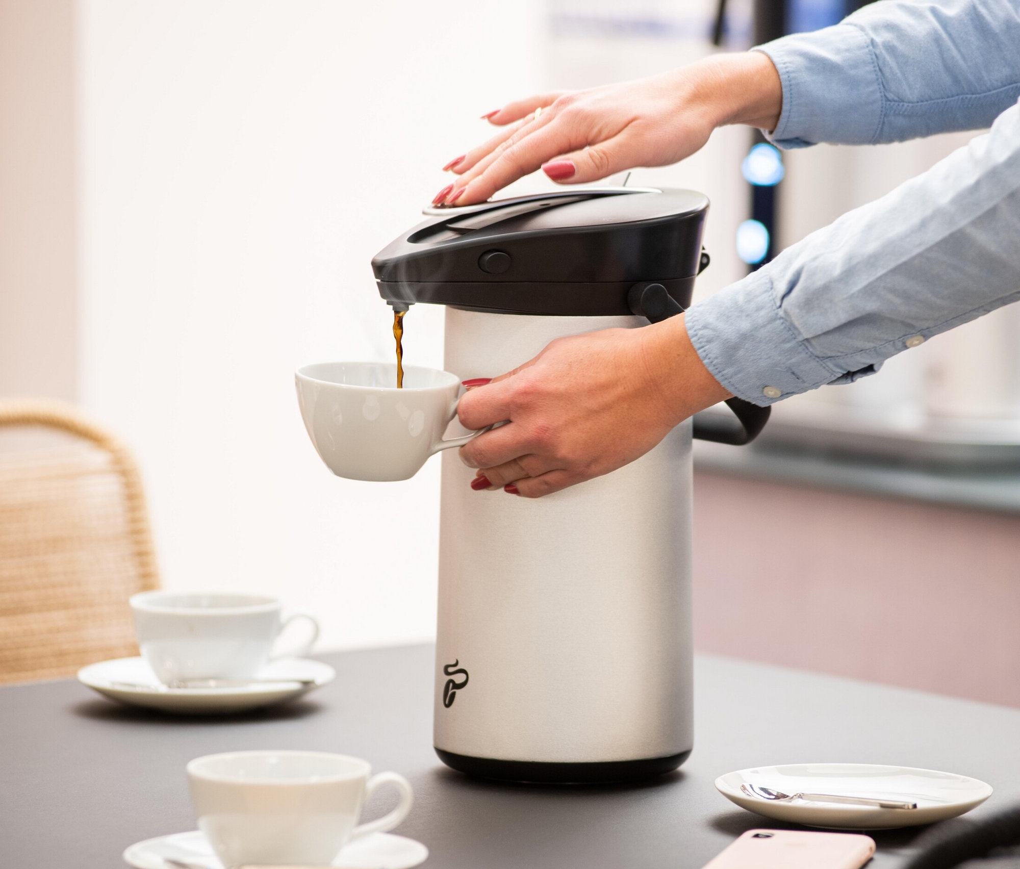 Frau gießt Kaffee aus einer silbernen Filbii 2L Thermoskanne in eine Tasse. Auf dem Tisch stehen weitere Tassen und Untertassen.