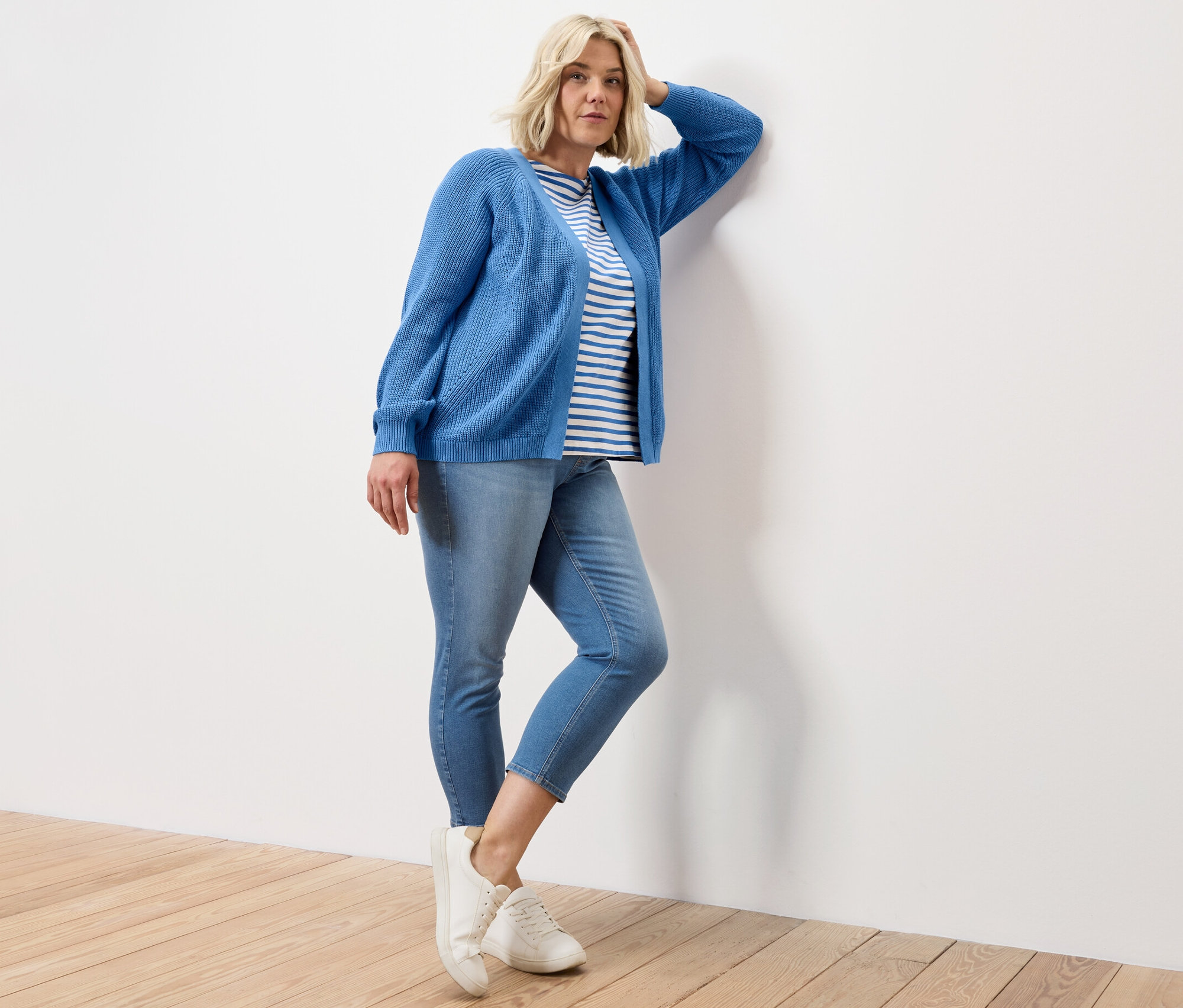Frau posiert an eine Wand gelehnt, mit blau gestreiftem Halbarmshirt, 7/8-Treggings – Fit »Nelly« und offenem Cardigan.