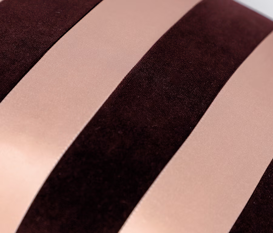 Detailaufnahme eines Kissens mit weinroten und rosa Streifen.