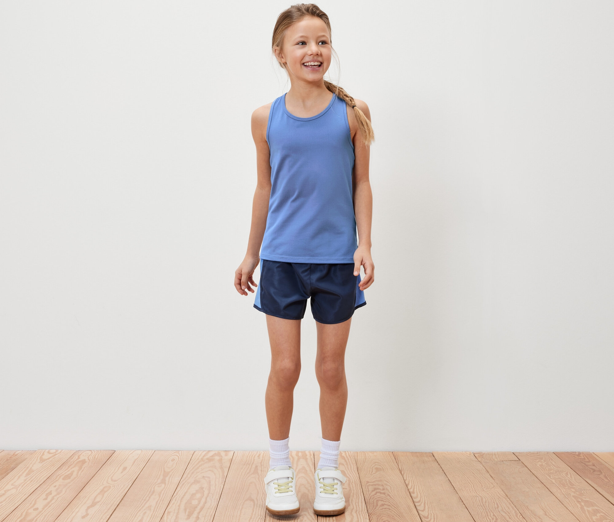 Lächelndes Mädchen steht und trägt ein blaues Sporttop und Sportshorts.