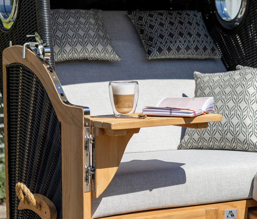 Detailansicht eines deVries Teak-Strandkorbs XL mit Kaffee und Buch.