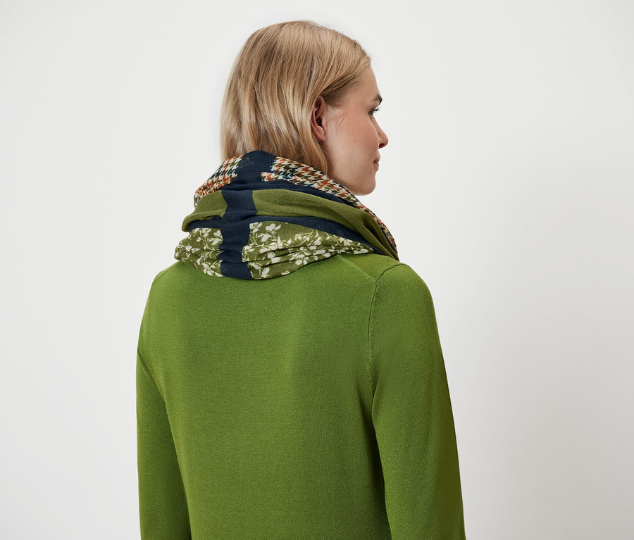 Frau mit blonden Haaren, grünem Pullover und Tuch um den Hals, von hinten gesehen.