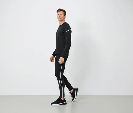 Mann in schwarzer Sportbekleidung mit reflektierenden Details geht auf grauem Boden.