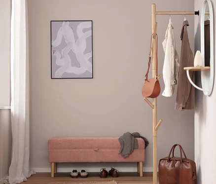 Flur mit rosa Bank, Schuhen, braunem Teppich, Garderobenständer, Handtasche und Spiegel.