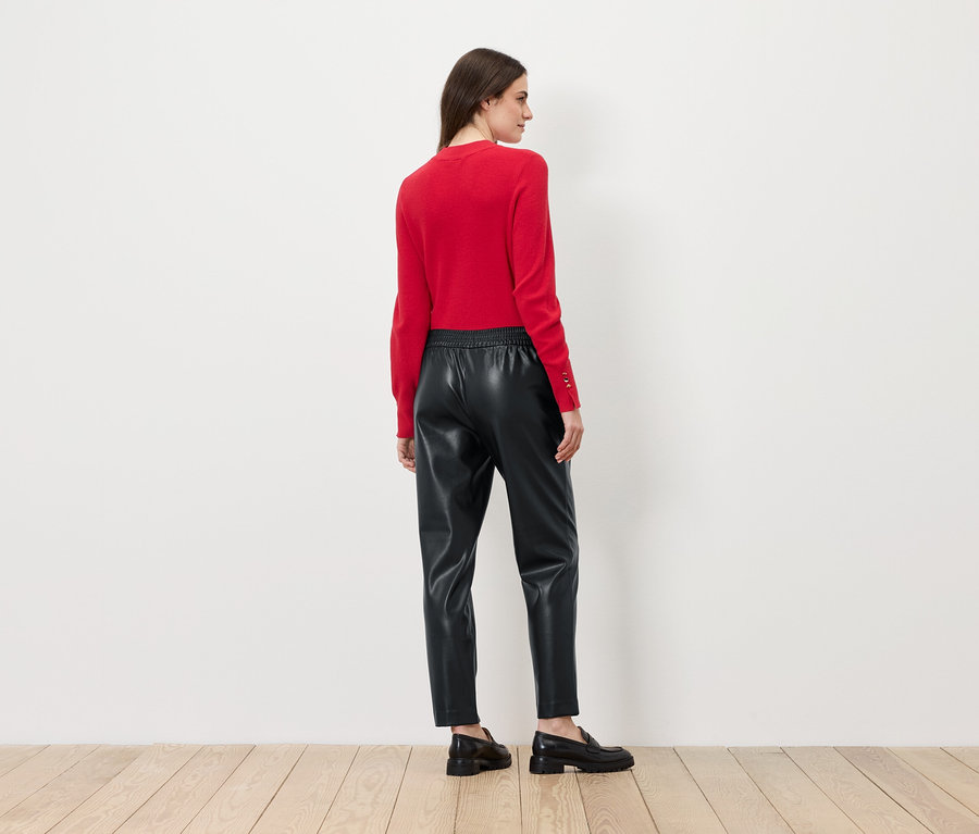 Frau mit dem Rücken zur Kamera trägt einen roten Pullover und eine schwarze Lederhose.