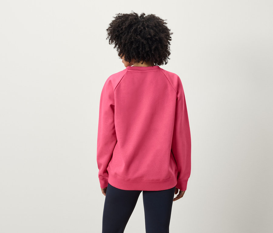 Rückansicht einer Frau mit Afro-Frisur in einem rosa Sweatshirt und dunkelblauen Hosen.