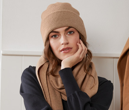 Frau sitzt auf einem Stuhl und trägt eine beige melierte Strickmütze.