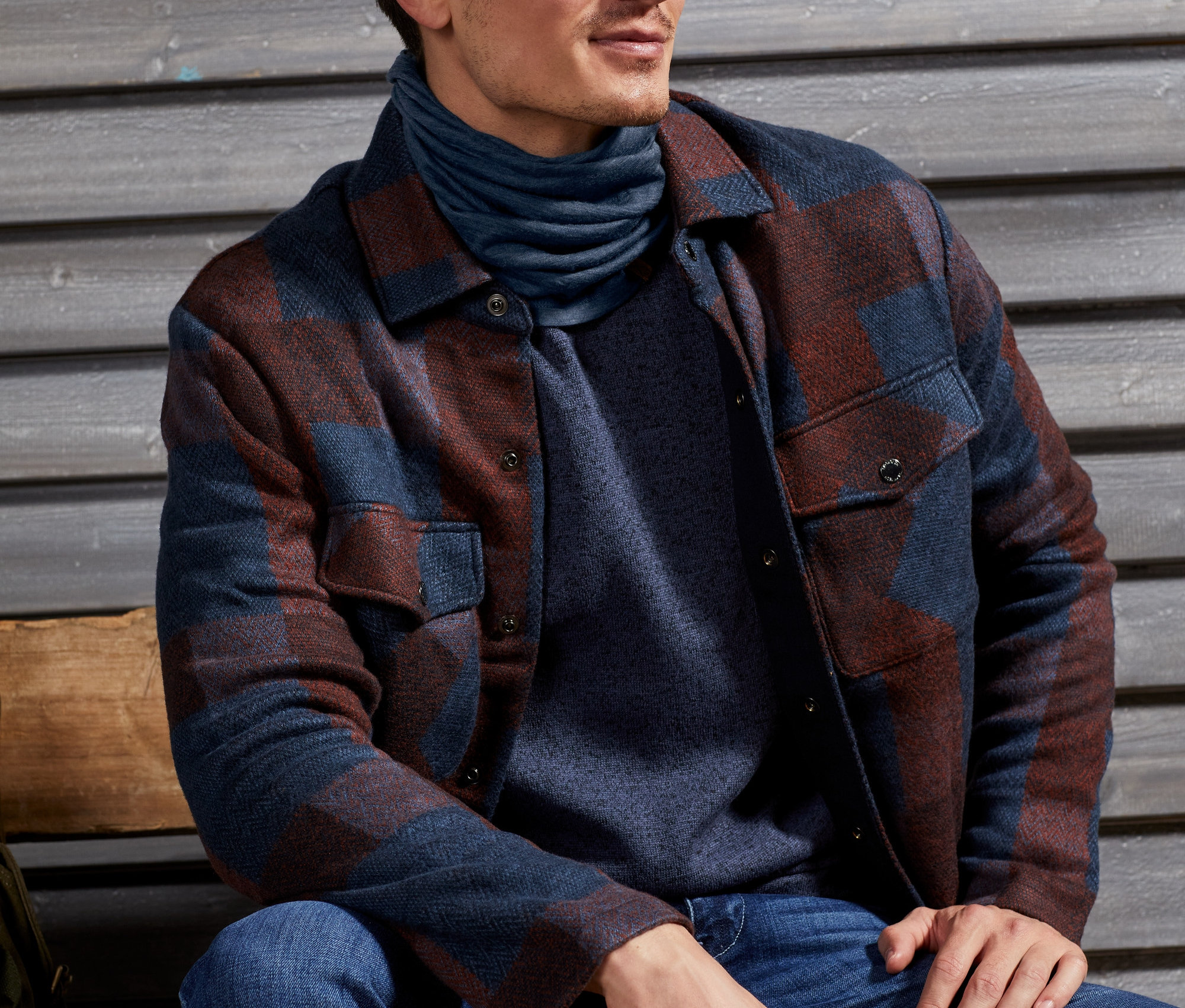 Mann sitzt und trägt ein Multifunktionstuch aus Merinowolle und eine Hemdjacke im Worker-Style.