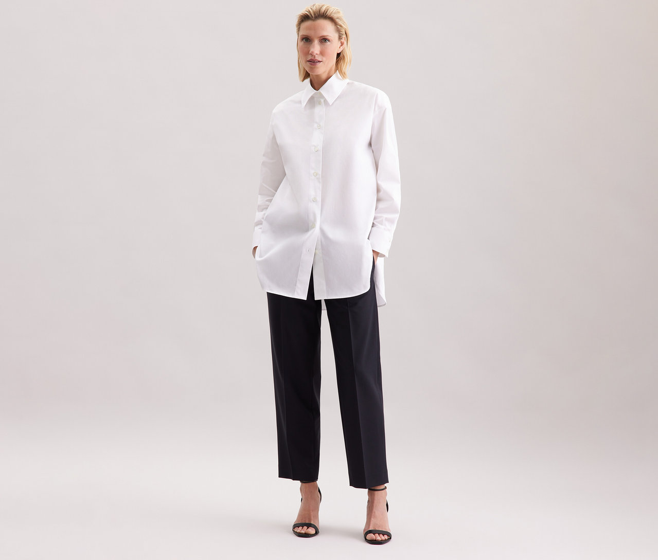 Frau mit einer weißen Seidensticker Oversize Longbluse und schwarzen Hosen.