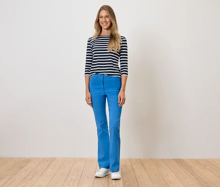 Frau steht und trägt blaue Hosen, ein gestreiftes T-Shirt und weiße Schuhe.